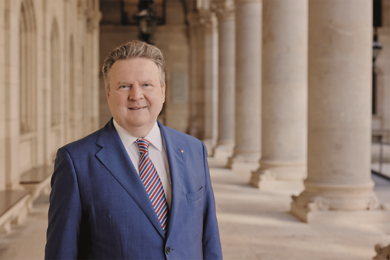 Formelles Porträt von Bürgermeister Dr. Michael Ludwig: Er trägt einen blauen Anzug, weißes Hemd und eine rot-blau gestreifte Krawatte.