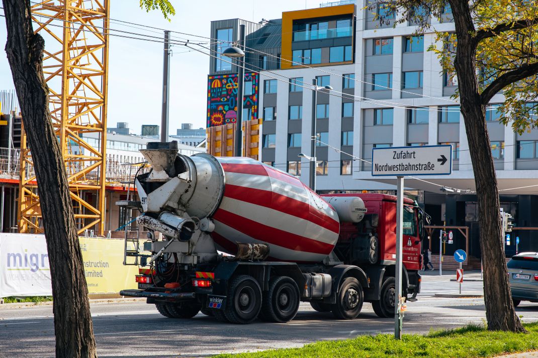 Es ist ein Fahrmischer im Nordbahnviertel abgelichtet. Der Mischer ist rot und weiß gestreift. Im Hintergrund sieht man den Anfang eines Baukrans. 