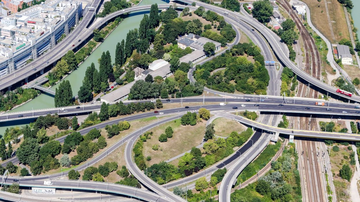 Kapitelbild: Ein Schrägluftbild, das Wien von oben zeigt: verflochtene Transportwege, im spezifischen Straßen, Gleise und die Donau wurden fotografiert. 