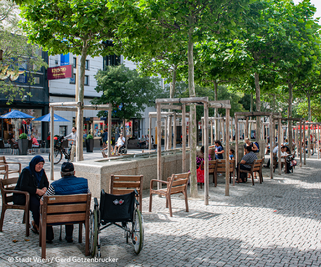Menschen in begrünter Fußgängerzone nutzen Sitzgelegenheiten