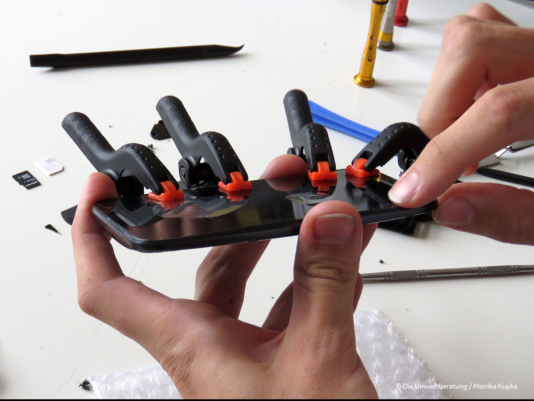 Detail einer Handyreparatur mit Händen und Halteklammern