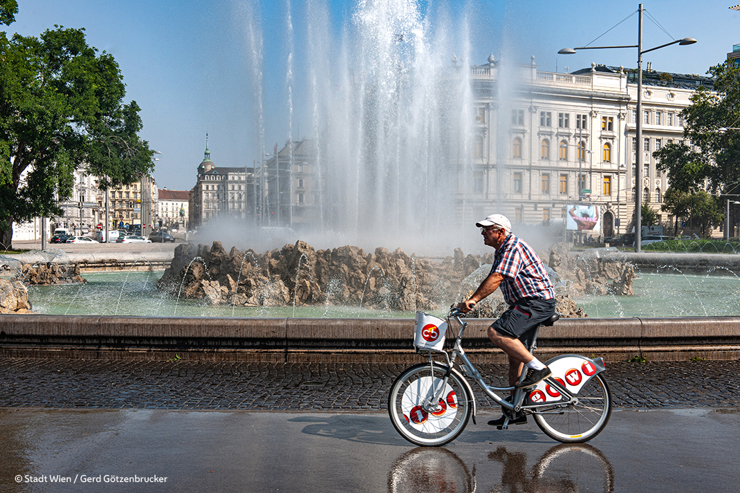 Mann auf einem Wien-Fahrrad fährt vor einem Hochstrahlbrunnen vorbei