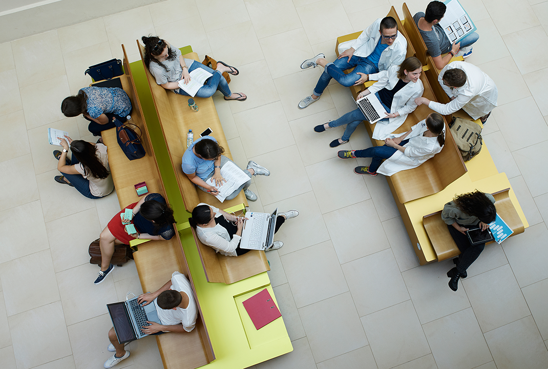 Lesende bzw. auf Laptops arbeitende Menschen auf Bänken von oben fotografiert