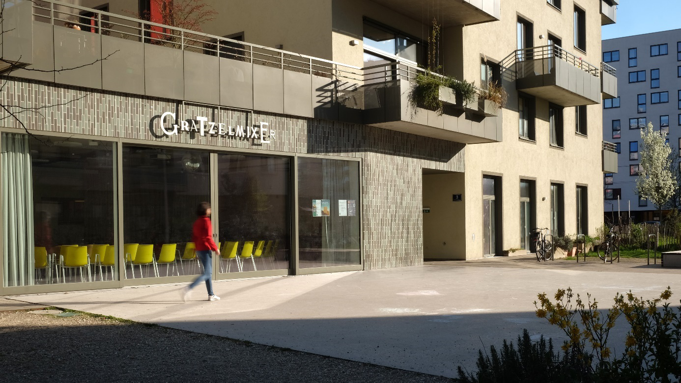Modernes Gebäude mit der Aufschrift „Grätzelmixer“, davor eine Fußgängerin.