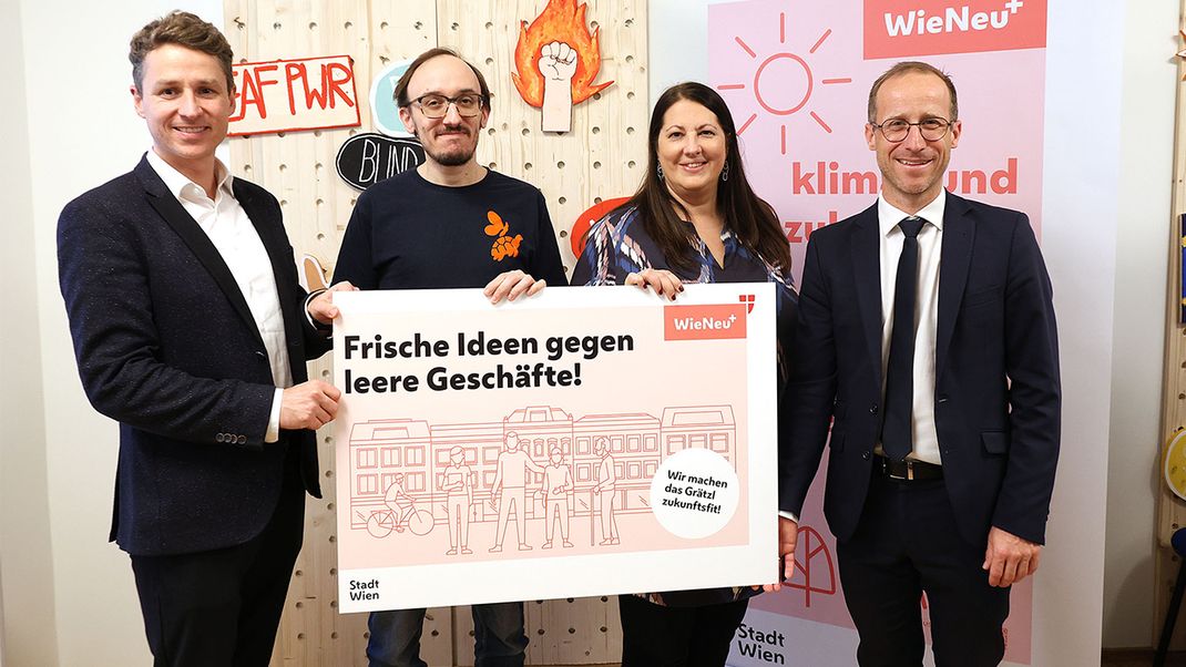 Four people – three men and one woman – are holding up an information board bearing the words ‘Fresh ideas to combat empty shops’ for the camera. To the right behind them is a roll-up banner featuring the Wieneu+ logo.