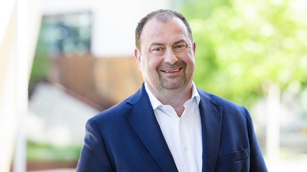 A portrait photograph of District Head Alexander Nikolai, smiling in a suit and white shirt.