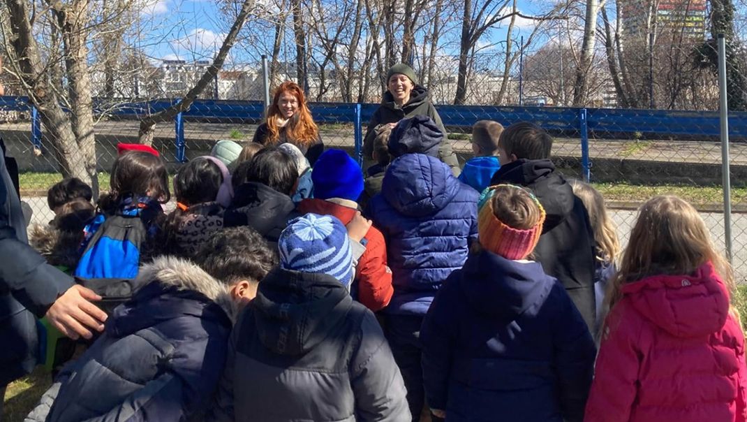 A group of primary school children are pictured from behind outdoors, facing two adult women teachers.