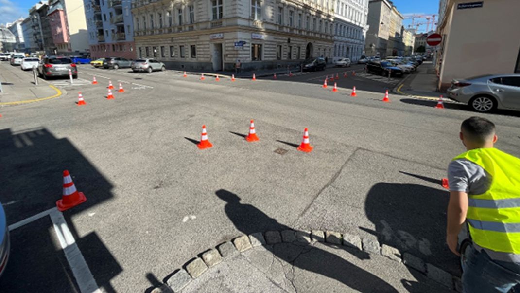 A wide-angle view of a road junction with a Gründerzeit-style house in the background. Red and white traffic cones mark out the safety zone.