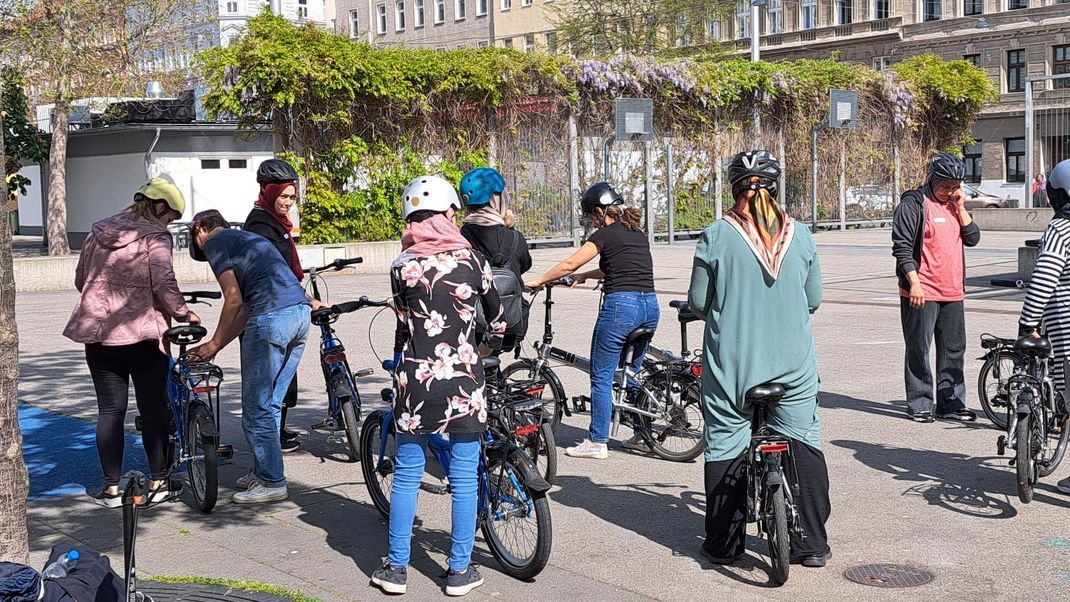 A group of women taking part in a cycling course. They are standing in a square and are being supervised by instructors.