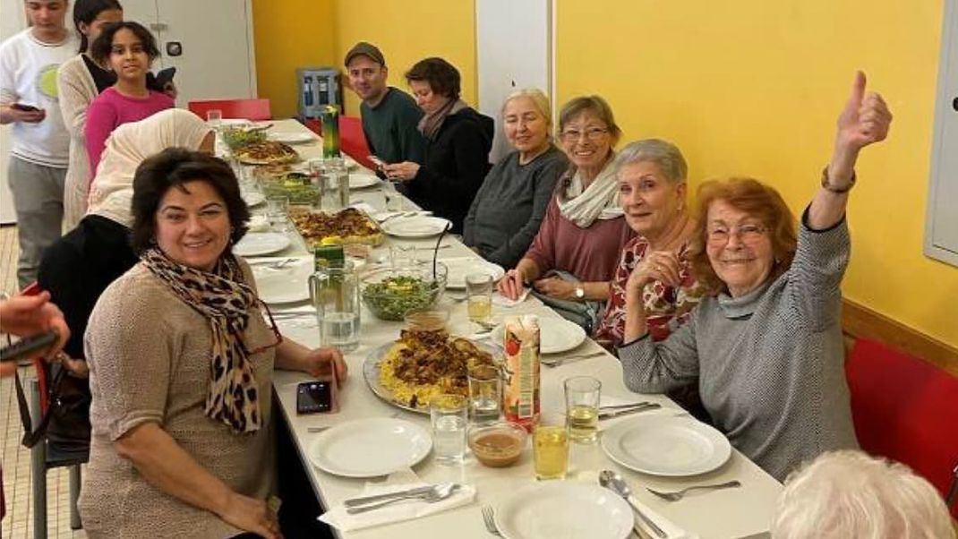 Participants in the events are seated at the laid table and are looking forward, in high spirits, to the meal they have cooked together.