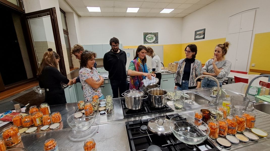 A bustling group of young people standing in front of saucepans and jars filled with carrots.