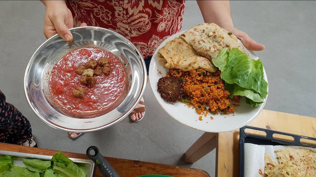 A woman, of whom only her two hands are actually visible, holds two plates of colourful Middle Eastern dishes up to the camera.