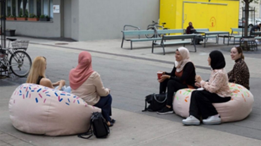 Women are chatting whilst sitting on cushions in a public space.