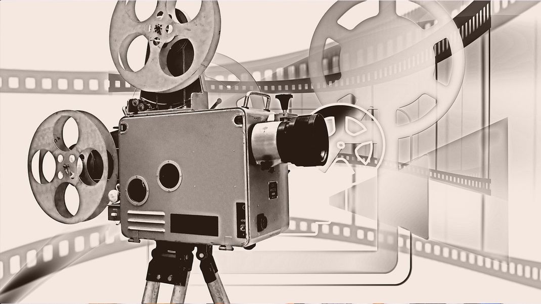 A depiction of a historic projection camera with film reels, rendered in pale dusky pink, grey and black.
