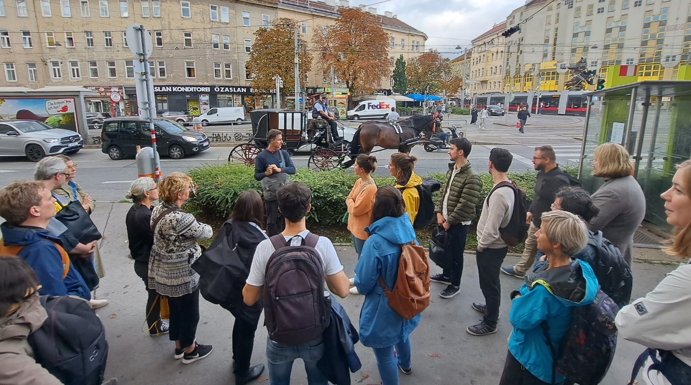 Cities4PEDs neighbourhood walk

A group of persons taking part in a neighbourhood walk on Quellenplatz square, with cars and a horse-driven cab - a Viennese "Fiaker" - as well as houses and trees in the background.