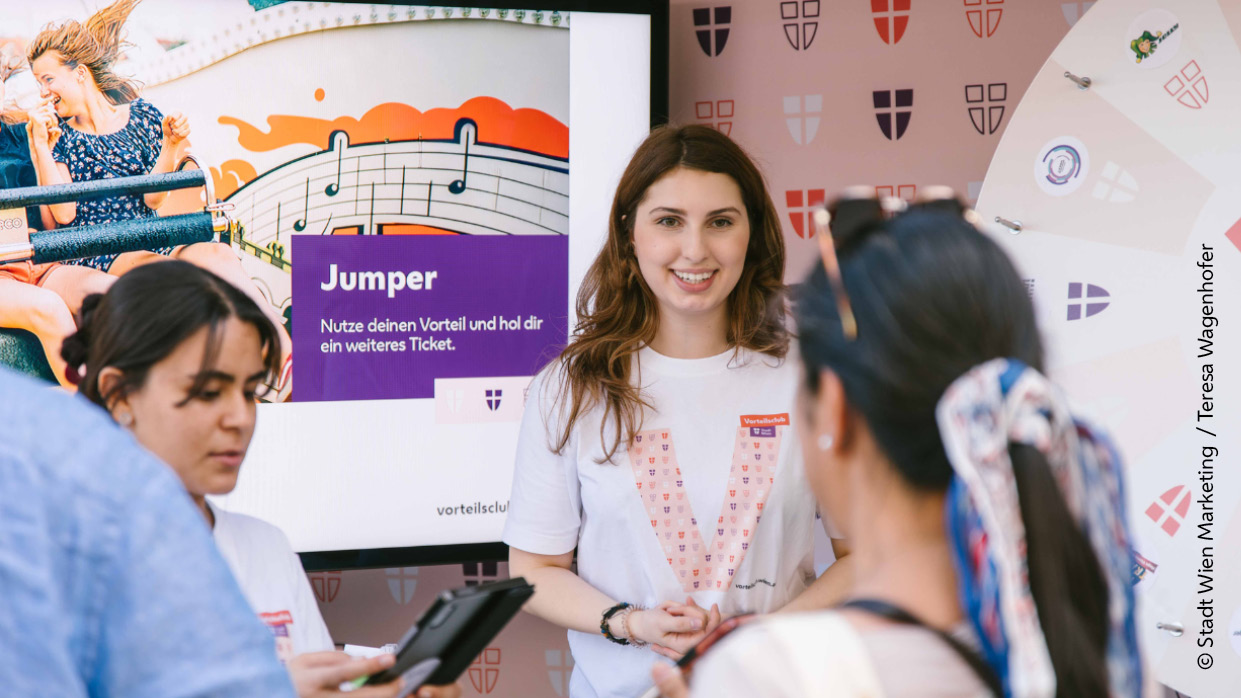 Kapitelbild: Fotografie eines Stand des Vorteilsclub der Stadt Wien mit drei Personen, von denen zwei im Vordergrund stehen.