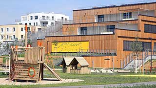 Ausschnitt des terrassierten Baukörpers. Die Fassade ist mit Holz verkleidet. Davor ist ein Spielplatz.