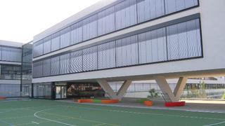 Blick vom Sportplatz auf die mit groen ffnungen versehene Fassade des die Freiflchen trennenden Gebuderiegels