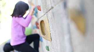 Detailauschnitt, rechts eine Betonwand mit Kletterelementen, im Hintergrund ein kletterndes Kind