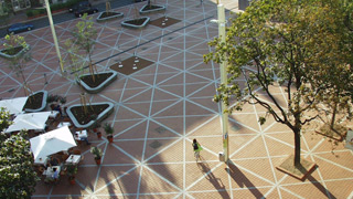 Blick von oben auf Platzbereich, Oberflche rot mit weien Linien, die Dreiecke bilden, rechts ein Baum, links Sonnenschirme