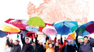 Gruppe frhlicher Menschen mit Regenschirmen in der Hand steht vor einem Plan der Stadt Wien