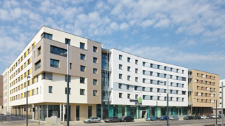 Straßenansicht des Studierendenwohnheims: mehrstöckiges, modernes Gebäude mit hohem Erdgeschoss