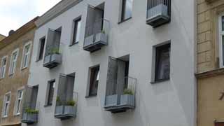Seitliche Straßenansicht auf dreistöckiges Gebäude zwischen Altbauten, versetzt angeordnete Balkone