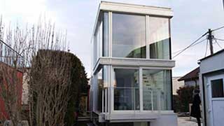 Ansicht auf schmales, zweigeschoßiges Haus mit Glasfronten