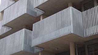 Seitenansicht auf drei Geschoße mit Balkonen, welche mit Metallelementen vertikal strukturiert sind