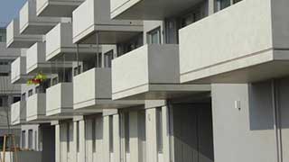Seitenansicht auf drei Geschoße eines Baukörpers mit kubischen Balkonen aus Sichtbeton