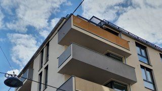 Eckansicht auf Gebäude mit heller Fassade und auskragenden Balkonen in unterschiedlichen gedeckten Farben