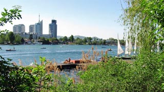 Jetty by the water, on the right are sailboats,  in the background a skyline