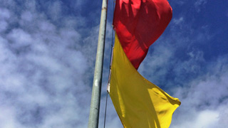 eine gelbe und eine rote Fahne an einem Mast