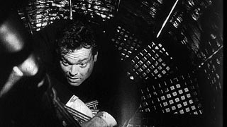 Black-and-white film still: Orson Welles on a spiral staircase