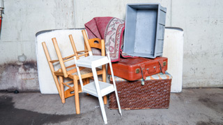 Sperrmll-Gegenstnde, darunter alte Sessel, Matratze, Koffer, Teppich, eine Truhe und eine Box, platziert vor einer weien Wand