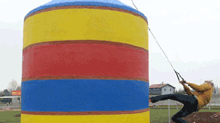Ein Mann hängt an einem Seil an einem großen bunten Zylinder