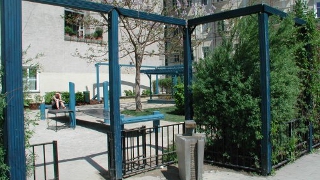 Parkeingang mit modernem Trinkbrunnen, blauer Pergola und einem niedrigen Zaun