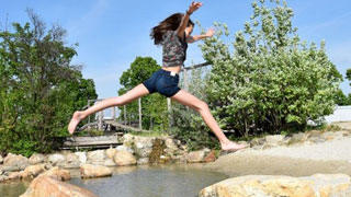 Mädchen springt über einen Bach