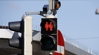 Red pedestrian traffic lights displaying two women who hold hands and wear a heart each
