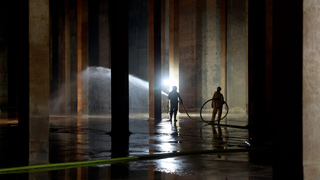 Wasserkammer mit Betonsäulen wird von 2 Personen mit Wasserschlauch gereinigt
