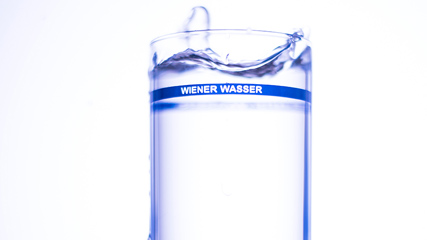 Hohes Wasserglas mit schmaler blauer Umrandung und Schriftzug "Wiener Wasser"